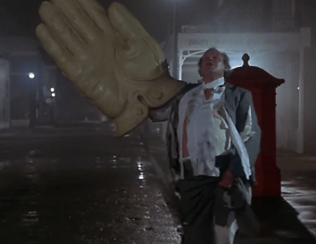 A man in a disheveled suit holding a large, oversized glove while walking on a dimly lit street at night.